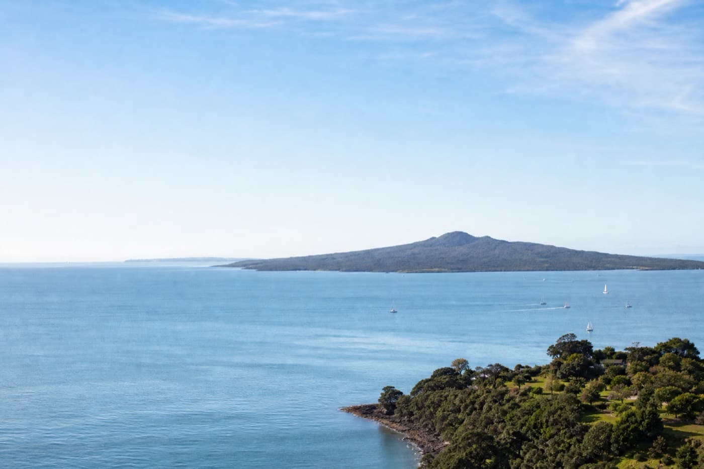 Auckland harbor with volcanic hills and sailboats under clear sky, New Zealand