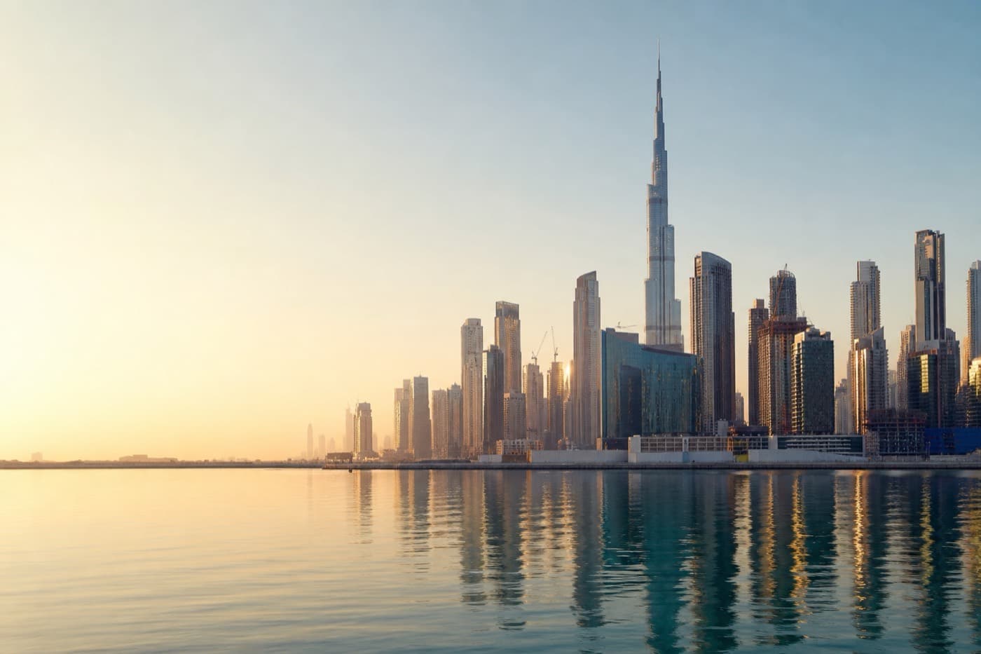 Dubai skyline and waterfront across calm Gulf waters at golden hour, UAE